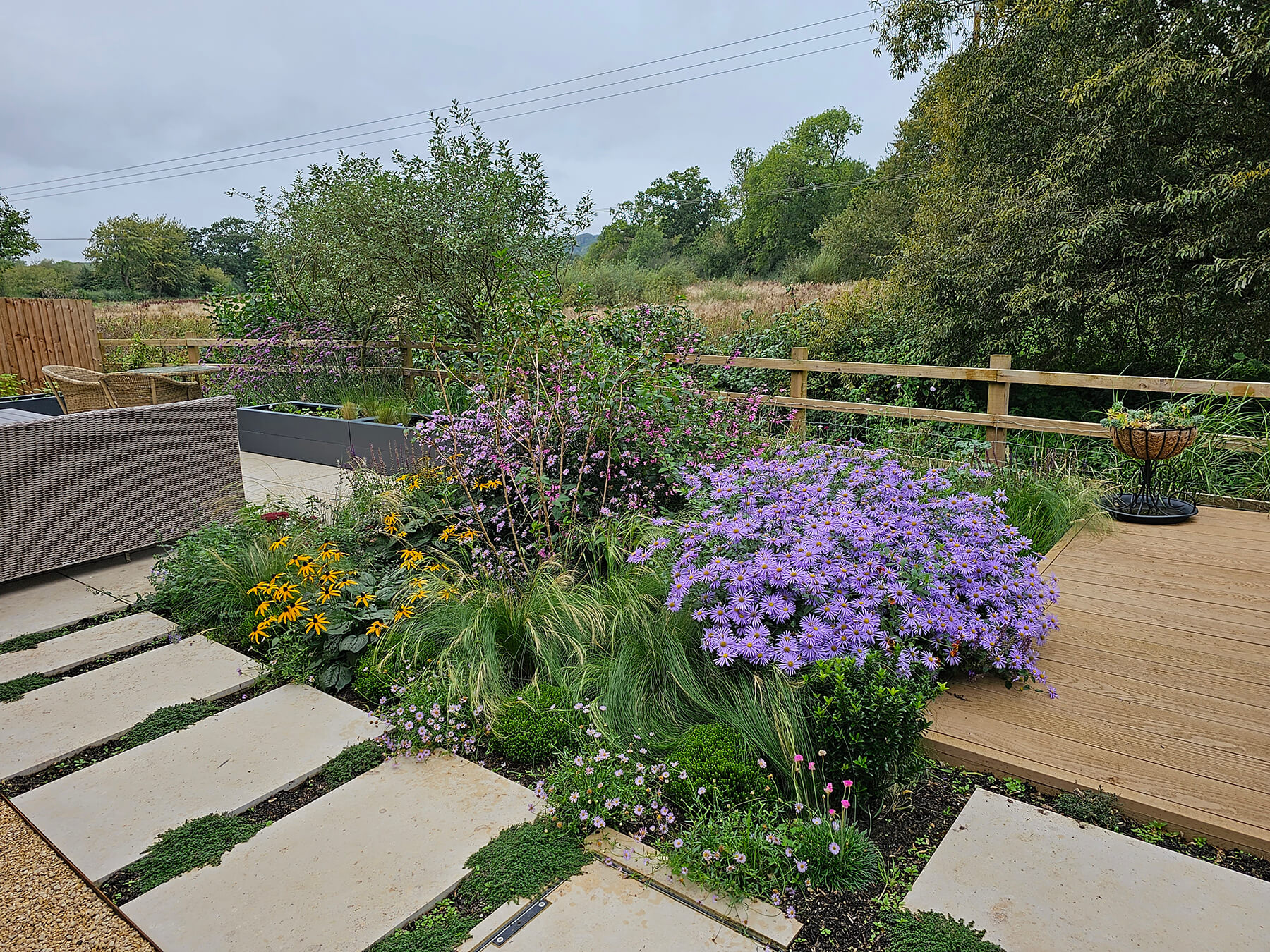 The Garden with a View, A new build garden plot redesigned to harness the view featuring planting to echo the landscape beyond, a sundeck and paving interplanted with thyme. Designed by April House – Award Winning Cotswolds Garden Design