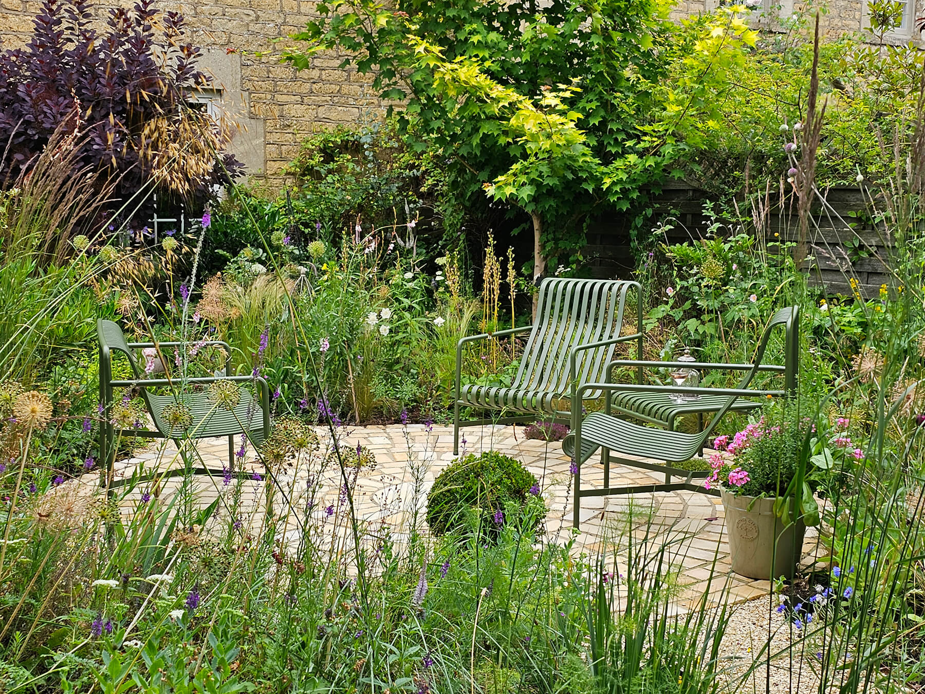 The No Lawn Front Garden, a Cotswolds cottage garden with circular sandstone seating area surrounded by naturalistic planting. Designed by April House – Award Winning Cotswolds Garden Design