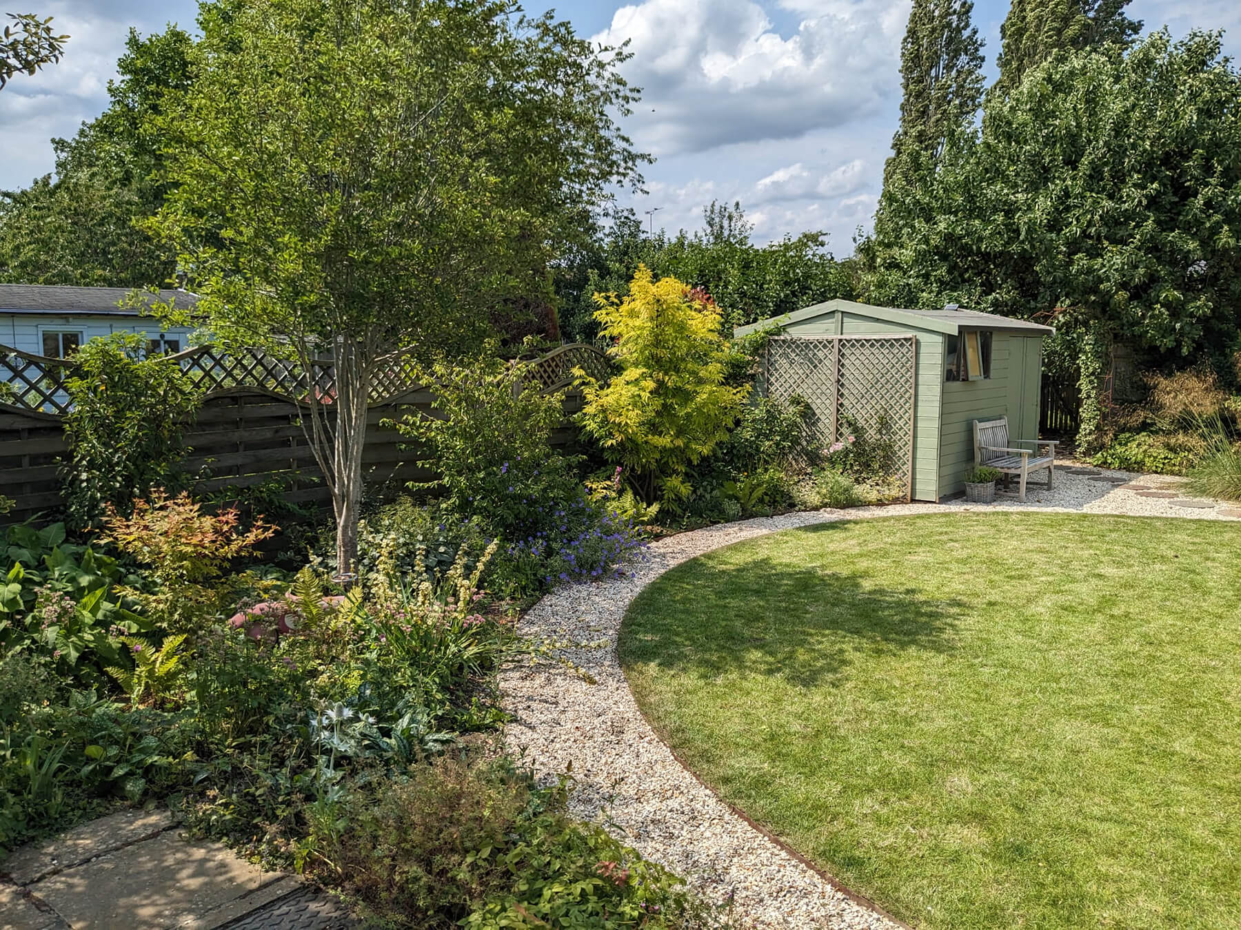 The Screening Garden, a garden design for screening solutions, featuring garden room, screening planting, lawn, circular pathway, borders, sun spot and seating. Designed by April House – Award Winning Cotswolds Garden Design